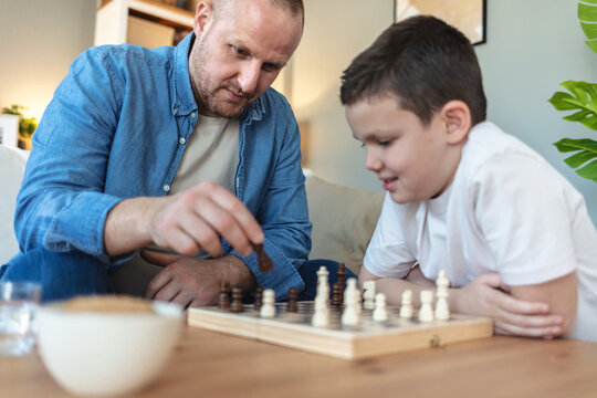 Playing, hands and father with kid for chess in home for learning, development or bonding. Teaching, competition and dad with boy child for board game with checkmate for problem solving skills. - Powered by Adobe