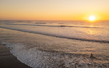 Sunset beach scene in Pimentel, Peru, with warm golden light, gentle waves and swimmers enjoying the ocean near the iconic pier. Perfect for travel and summer tourism content