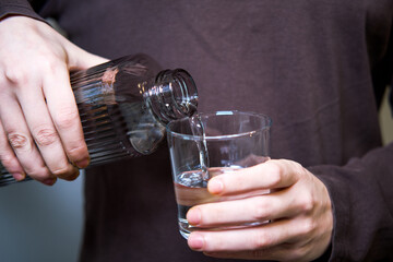 Man's hand pouring water from a jug into a transparent glass.