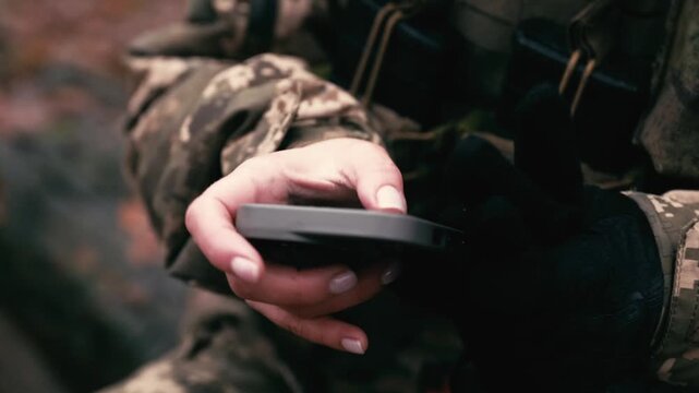 Detailed close-up of a woman in military uniform using a smartphone to type a text message. Focus is on her hands and the device, suggesting communication, duty, or a personal moment during deployment