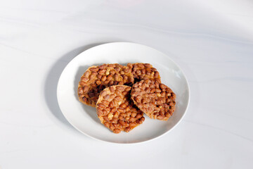 Peanut brittle placed on a white plate with a minimal light background, suitable for food, dessert, and traditional ingredient content