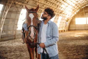 In casual clothes, standing by. Man is with horse in the hangar