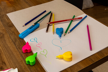 Children’s drawing scene with colored pencils, sharpeners and a sheet of paper filled with simple...