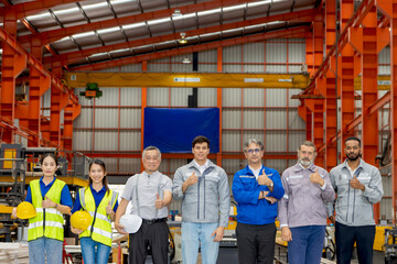Group of happy engineers standing line up in manufacturing factory. Corporate engineering workers give thumbs up while stand confidently in industrial setting. Diverse professional team look at camera