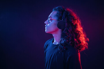 Long hair, headphones, side view. Guy is indoors at night with neon lighting