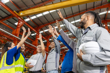 Group of happy engineers raise hands to celebrate together while stand in manufacturing factory. Cheerful corporate engineering diverse team raising hands up in industrial site. teamwork celebration