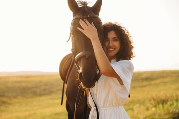 Fototapeta premium Against the horizon background. Woman in white dress is with horse on the countryside field