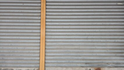 Old silver metal rolling door has rust and small scratches on the surface. The bottom has corrosion and decay. Metal plate wall texture and background.