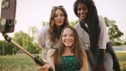 three multiracial female friends one disabled in a wheelchair enjoying a sunny day outdoors while capturing memories with a selfie stick in a park setting