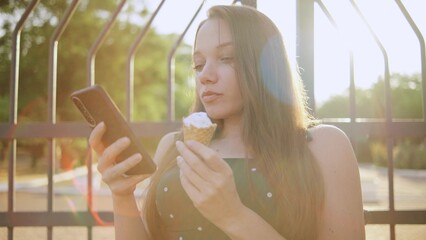disabled woman in a wheelchair enjoying ice cream while using smartphone in sunny park