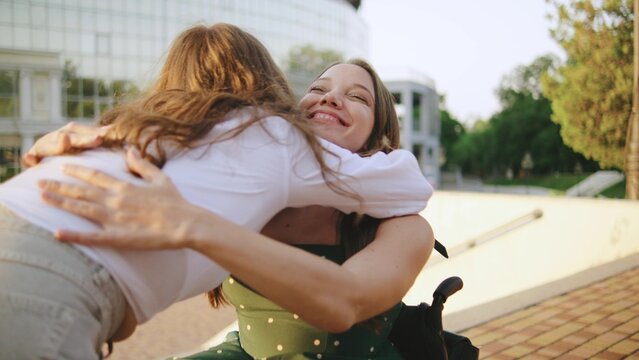 two female multiracial friends one inclusive woman in a wheelchair share a warm embrace outdoors as a disabled woman in a wheelchair enjoys a joyful moment in the sun - Powered by Adobe