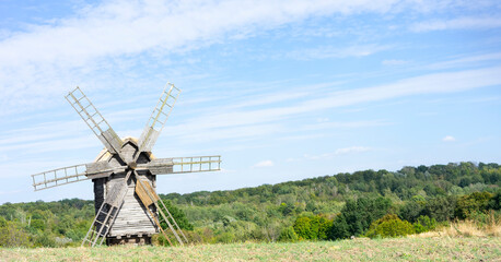 Old medieval windmill stands in a serene field surrounded by lush greenery under a clear blue sky