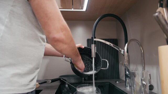 Man pouring water from a colander into a sink, showcasing kitchen activity with flowing water, camera follows the action with a smooth handheld movement