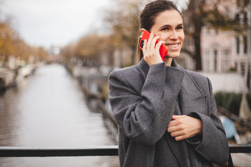 Happy young woman talking over mobile phone standing on bridge canal.  Call conversation....