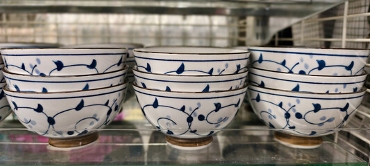 Stacked ceramic bowls with intricate blue floral patterns on white glaze, displayed on a glass shelf.Traditional vine motif encircles each bowl, showcasing symmetrical leaf and dot detailing.