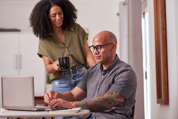 Friends At Home Office: Man Working On Laptop While Woman Drinks Coffee And Watches