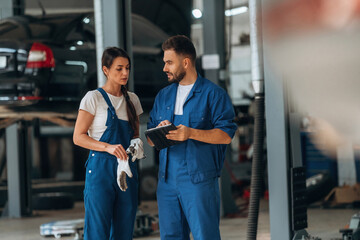 Digital tablet is in hands. Auto repair shop employees are working together. Man and woman