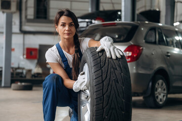 Seasonal replacement conception. Woman mechanic is with tire in the modern car workshop