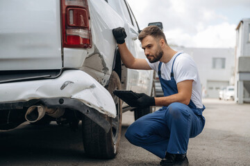 Assesses damage. Mechanic is sitting by the damaged pickup truck outdoors © standret
