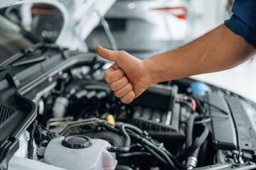 Done, showing thumb up, hood is opened. Close up view of male service station worker at job