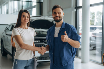 Deal, doing handshake. Woman customer is in the car repair service station with mechanic