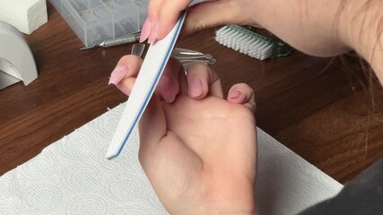 Woman performing a DIY manicure at home, carefully cleaning nails with a brush for self-care and manicure by yourself, using nail care tools on a wooden table
