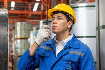 Portrait of male worker with safety clothing and helmet hold walkie during inspecting large metal tube in industrial site. Engineer work at manufacturing factory. Inspector checking quality of product
