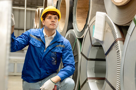 Male worker with safety clothing and helmet inspecting large metal tubes in industrial site. Engineering staff working at manufacturing factory. Inspector checking the quality of metal sheet product - Powered by Adobe