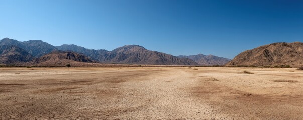 Dry desert plain with cracked earth and rugged mountain ranges under a clear blue sky, ideal for nature themes, travel visuals, environmental concepts, and cinematic scenic backgrounds
