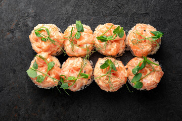 Gourmet salmon sushi rolls topped with fresh raw salmon tartare and microgreens on sesame-coated rice, elegantly styled on dark slate. Premium Japanese cuisine, luxury salmon maki, seafood sushi.