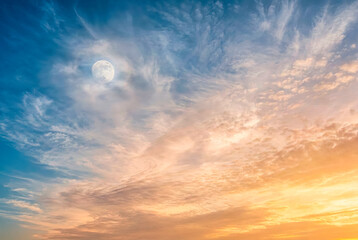 Obraz premium Ethereal blue and orange sunset sky with full moon and wispy clouds, dramatic twilight atmosphere background