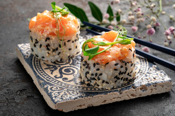 Two creamy salmon sushi rolls topped with rich salmon tartare and microgreens, elegantly served on an ornate plate with chopsticks. Luxury Japanese maki, premium creamy salmon roll.