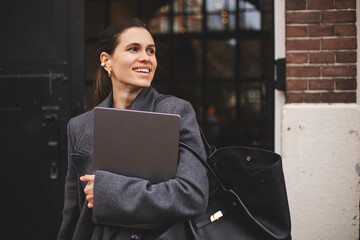 Confident high ponytail businesswoman wearing grey wool coat, sweater go with a laptop in hand....