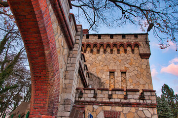 Kamienna wieża zamkowa z łukiem z czerwonej cegły pod czystym niebem i drzewami. © Pol Badger