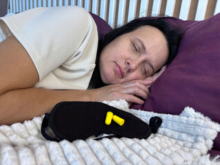 Sleeping adult woman with sleep mask and earplugs beside her, concept of peaceful rest and noise protection