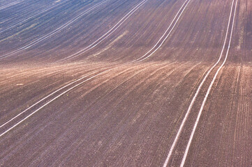 Widok z lotu ptaka na zakrzywione bruzdy na świeżo zaoranym polu ozimego zboża. Ciepłe, ziemiste barwy i subtelne faktury oddają rytm wiejskiego rolnictwa. © Pol Badger