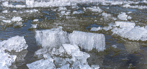 Clear ice blocks are scattered across the water surface, reflecting sunlight in a serene winter landscape, showcasing the beauty and tranquility of nature during the cold season