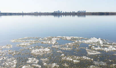 Tranquil lake scene featuring floating ice fragments on the surface, reflecting a distant skyline under a clear blue sky, creating a serene and peaceful atmosphere in nature