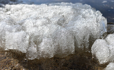 Close-up view of ice formation along a rocky shoreline, showcasing glistening textures and natural beauty, with sunlight reflecting off the ice, creating a serene winter atmosphere