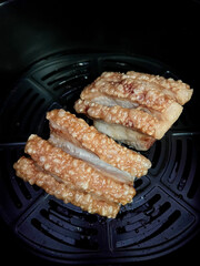 Crispy pork belly crackling with golden bubbly skin served in air fryer basket, savory and crunchy