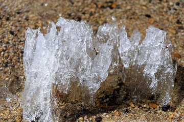 Intricate ice formation rests on sandy beach, showcasing a blend of textures and colors. The sunlight highlights the transparent edges, creating a stunning visual contrast with the sand