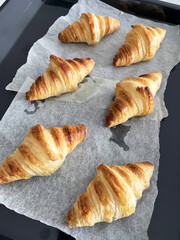 Fresh baked croissant pastry on parchment paper with golden flaky layers, cozy breakfast aroma and warm texture