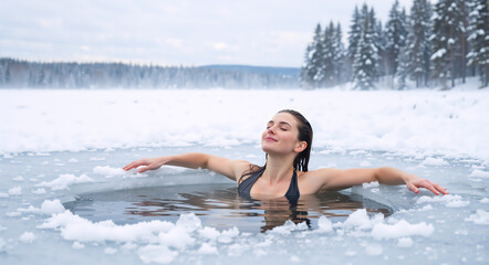 Fototapeta premium Happy woman enjoying winter swimming in frozen lake. Ice bathing for health and wellness. Snowy forest landscape