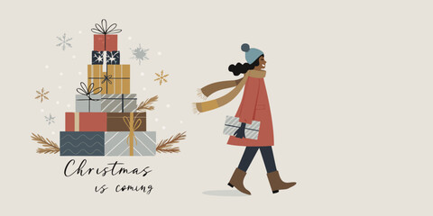 A woman carrying christmas gifts walking past a pile of presents