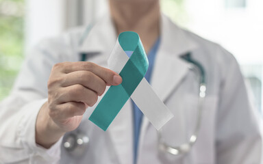 Teal and white ribbon for cervical cancer awareness month in January and HPV prevention with bow on medical doctor's hand support
