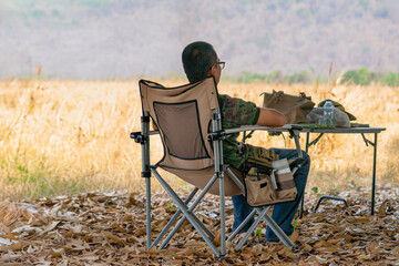 Back view of man tourist sit alone on camping chair in dry field. Man resting after long day of hard farm work, solitude and peaceful contemplation at end of day. Relaxation traveling in park concept.
