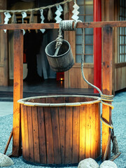 Wooden bucket and rope with beautiful artesian well made by wood and wheel pulley in front of house. Retro wooden water well in rural area. Garden decoration with Japanese style antique items.