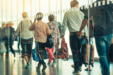 Photograph through large clear glass wall with blurred image of departing passengers and luggage walking airplane boarding corridor from terminal to plane in background. Selective focus on glass.