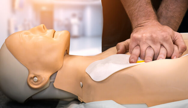 Defibrillator AED CPR emergency first aid training demonstration - cardiopulmonary resuscitation medical procedure on dummy. Teaching chest compression technique to student learning via mannequin doll