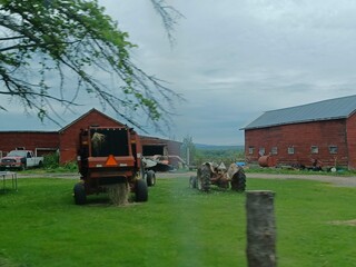 Rural Scenery of a small farm with tractors, red barns and open fields on a cloudy day.